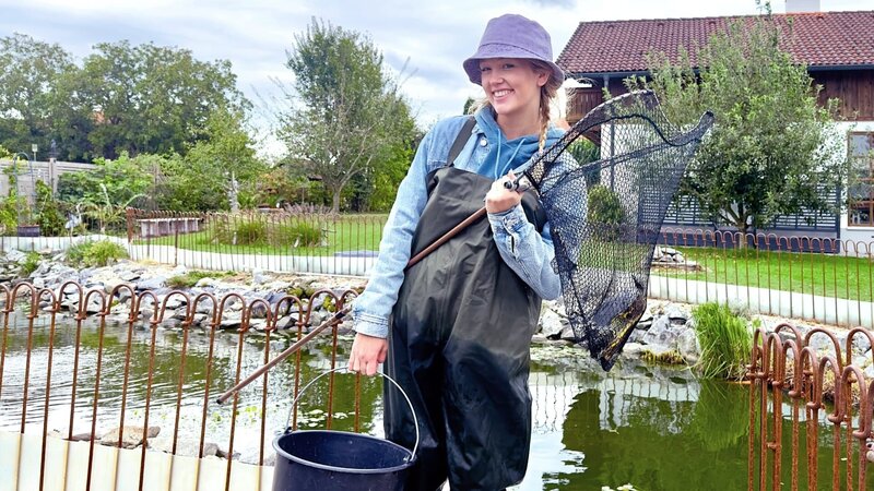 Um die Schildkröten einzufangen, geht es für Nina mit Wathose, Eimer und Kescher ab in den großen Teich. Mal sehen, wie viele Schildkröten ihr ins Netz gehen. – Bild: BR/​BILD+TEXT Medienproduktion GmbH & Co. KG/​Katharina Brackmann