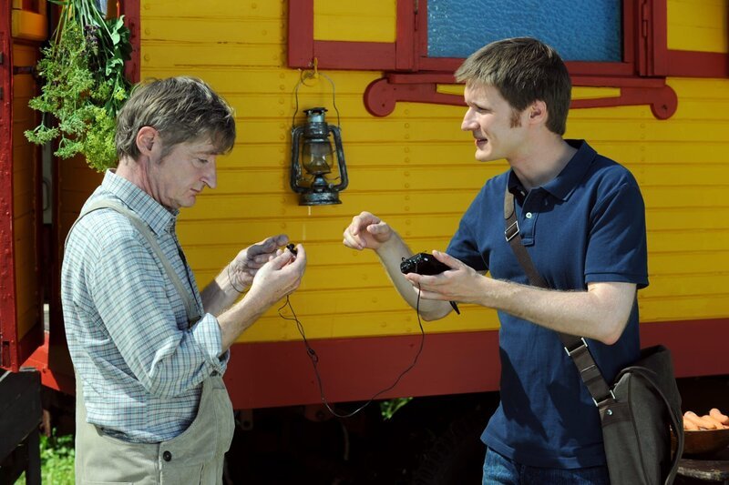 Ludwig gibt Xaver einen Walkman, der ihm beim Lernen des Textes helfen soll. Von links: Xaver (Michael Schreiner) und Ludwig Brunner (Martin Wenzl). – Bild: Marco Orlando Pichler /​ BR /​ BR/​Marco Orlando Pichler