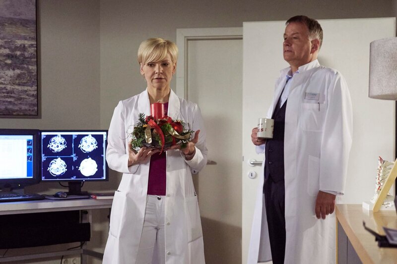 Dr. Kathrin Globisch (Andrea Kathrin Loewig) räumt aus Rücksicht auf seine Allergie, den Weihnachtsschmuck aus Dr. Roland Heilmanns (Thomas Rühmann) Büro. Roland versucht sie scherzhaft des Diebstahles zu bezichtigen – doch beide wissen, dieses Jahr ist alles anders. Es wird das erste Weihnachten ohne Pia Heilmann, Rolands Frau. – Bild: MDR/​Saxonia Media/​Wernicke