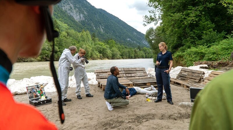 Caro Reisser (Sarah Thonig, r.) teilt Jerry Paulsen (Peter Marton, M.) die Todesursache und den Todeszeitpunkt des Opfers mit (mit Kompars:innen). – Bild: ARD/​Lucky Bird Pictures/​Savoy Film Productions