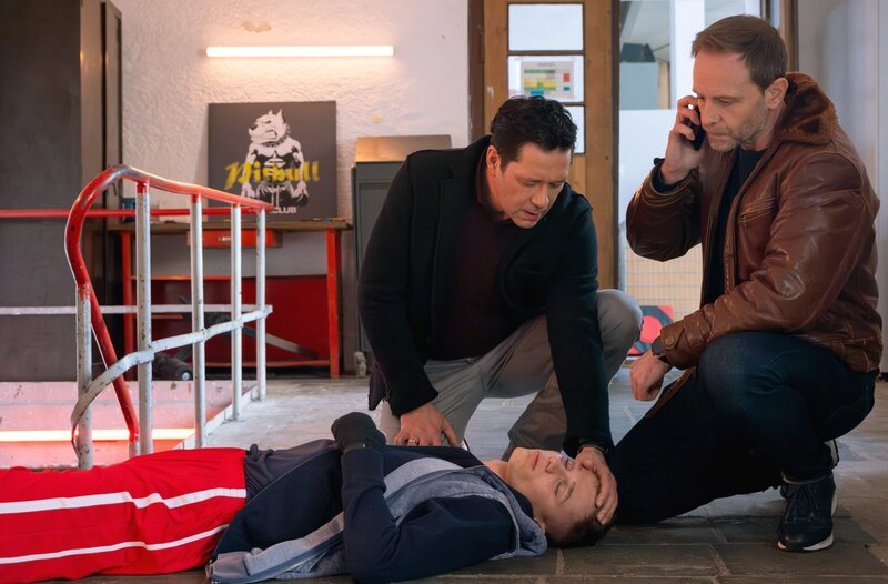 Dr. Kai Hoffmann (Julian Weigend, re..) und Dr. Philipp Brentano (Thomas Koch, li.) finden Finn Mohrbach (Tristán López, liegend) tatsächlich in seinem Boxclub. Als sie ihm sagen, dass er sehr wahrscheinlich eine lebensgefährliche Hirnblutung hat, läuft er davon und bricht zusammen. – Bild: MDR/​Saxonia Media/​Sebastian Kiss