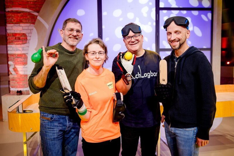 Beim Tischballspielen kommt es nicht nur auf die Schlagkraft an, sondern auch auf ein gutes Gehör. Schiedsrichter Michael Heuer (l.), Tischballspielerin Bianca Schmidt und Tischballspieler Stefan Lohmaier (r.) stellen Elton (2.v.r.) und dem Publikum ihren Sport vor. – Bild: ORF/​ZDF/​Nadine Rupp