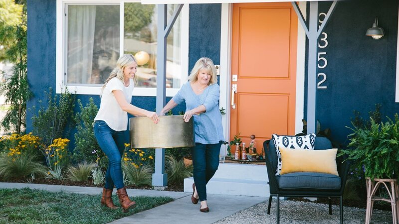 Jasmine (L) and Betsy (R) help each other carry a gold coffee table out to the lounge area where they will add refreshing beverages and lively plants. – Bild: Scripps Networks, LLC