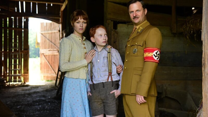 Felix (Xari Wimbauer, M.) ist gleichermaßen erschreckt wie fasziniert von Ortsgruppenleiter Feik (Philipp Hochmair, r.). Seine Mutter Anna (Lisa Wagner, l.) sieht das mit großer Sorge. – Bild: ZDF und Jürgen Olczyk