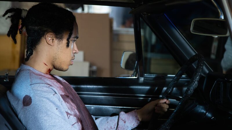 CALEB, heavily injured and in pain, as he’s looking at the rear mirror – Bild: Warner Bros. Discovery, Inc. or its subsidiaries and affiliates