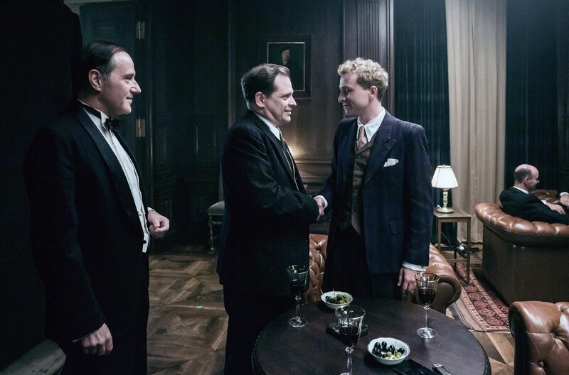 Über seinen Schwiegeronkel Carl (Stefan Kurt, li.) macht Johann (Max Hubacher, re.) Bekanntschaft mit einflussreichen Geschäftsmännern, von denen er sich finanzielle Unterstützung für sein Unternehmen erhofft. – Bild: SRF/​Sava Hlavacek