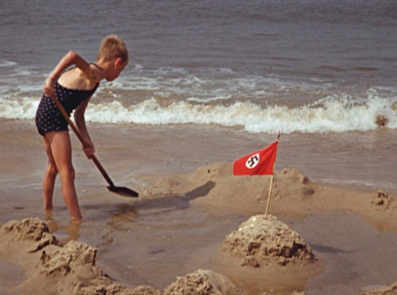 Junge baut Sandburg mit Hakenkreuz-Fähnchen am Strand. – Bild: phoenix