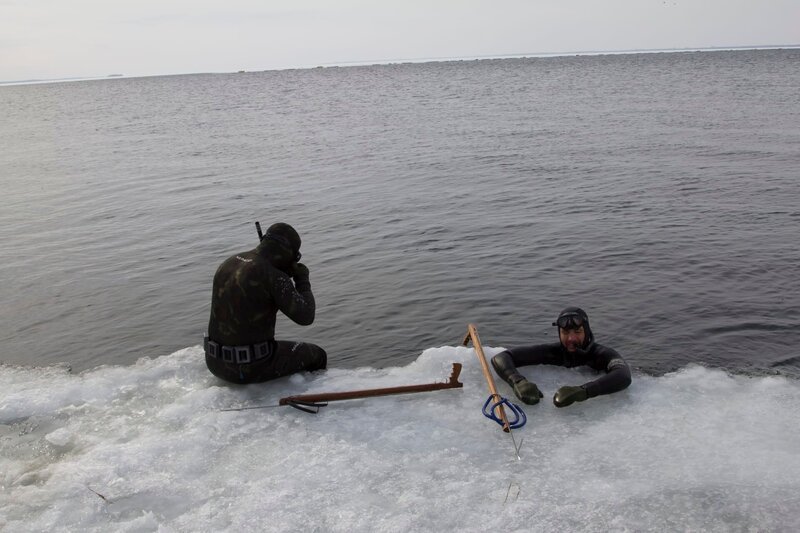 Eric sitting on the ice. Rene Potvin inside the water. Their spears near them on the ice. – Bild: Discovery Communications, Inc.