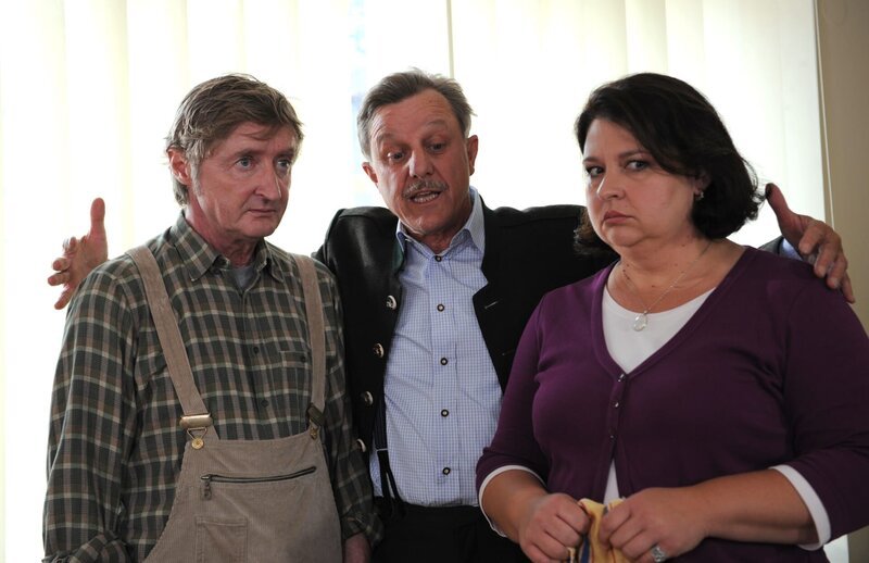 Bürgermeister Schattenhofer klärt Xaver und Monika über seine vertrauensbildenden Maßnahmen auf. Von links: Xaver (Michael Schreiner), Bürgermeister Schattenhofer (Werner Rom) und Monika Vogl (Christine Reimer). – Bild: Marco Orlando Pichler /​ BR