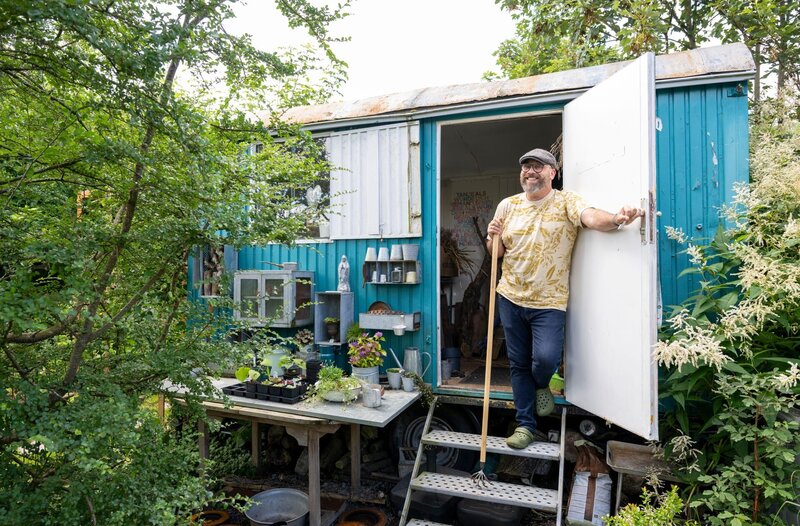 Freudenberg im Siegerland: Hier hat Peter Mecklenburg einen schmalen Hausgarten in ein überraschendes Gartenparadies voller Pflanzen und Deko-Objekte verwandelt. Auf 750 Quadratmetern hat er gemeinsam mit seinem Mann Ben zusätzlich ein Gewächshaus für Gemüse gebaut und einen türkis gestrichenen Bauwagen aufgestellt. – Bild: WDR/​Melanie Grande