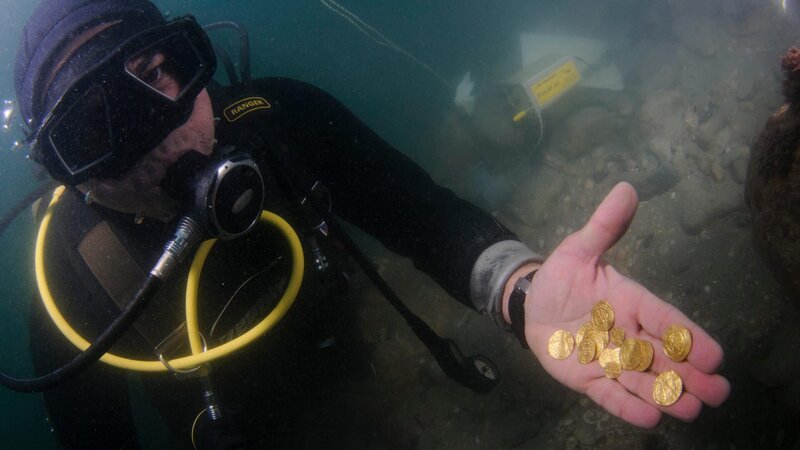 Underwater shot of a diver holding gold coins. – Bild: Alamy Stock Photo