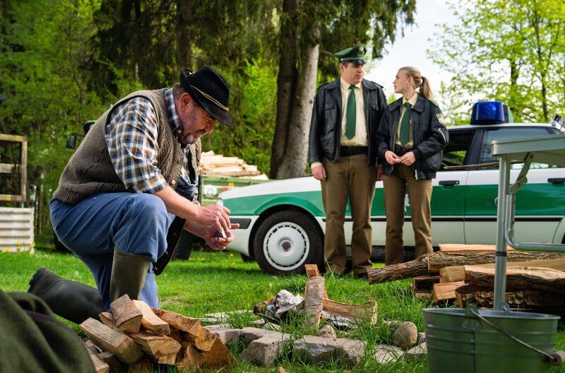 Förster Rappenglück (Peter Rappenglück, l.) will den umgestürzten Baum zu Riedls (Paul Sedlmeir, M.) und Rebeccas (Jeanne Gouraud, r.) Entsetzen gleich weiter verwenden. – Bild: ARD/​BR/​TMG/​Arvid Uhlig