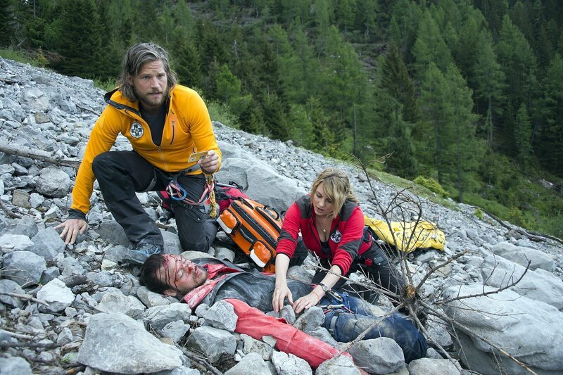 Die Bergretter Markus (Sebastian Ströbel, l.) und Katharina (Luise Bähr, r.) finden den abgestürzten und schwer verletzten Jan Fugain (Patrick G. Boll, M.). Während Katharina Strasser ihn erstversorgt, erkennt Markus, dass der Patient kein Unbekannter ist. – Bild: ZDF und Thomas R. Schumann