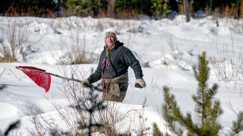 Cody Lundin stands in a snowy field using a red bandana on a stick to signal help. – Bild: Discovery Communications
