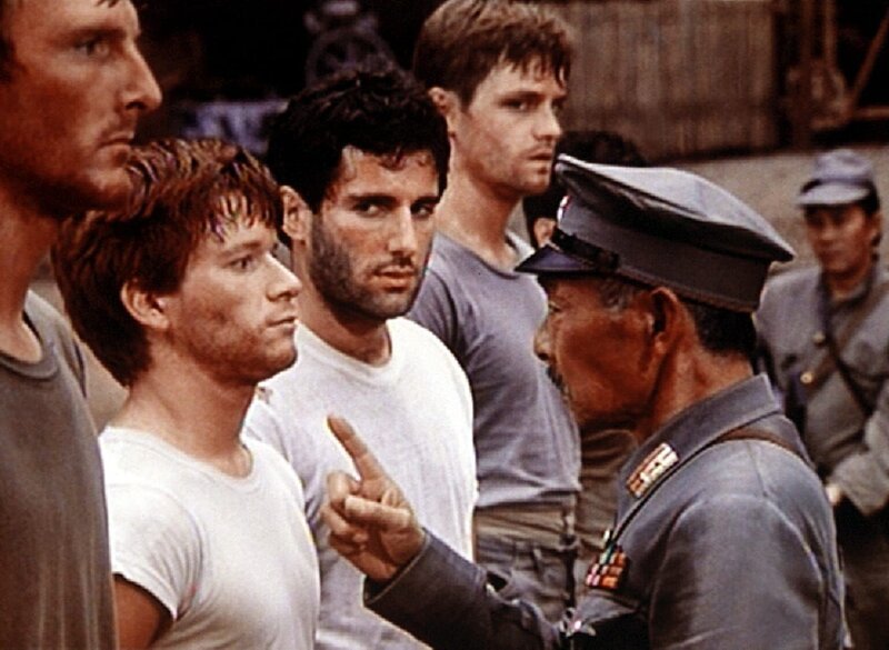 Ben (Eric Scott, 2.v.l.) und Norman (Jordan Suffin, 3.v.l.) werden von dem japanischen Kommandeur (Jerry Fujikawa) dabei überrascht, als sie in dem Gefangenenlager die amerikanische Flagge hissen. – Bild: WARNER BROS. INTERNATIONAL TELEVISION