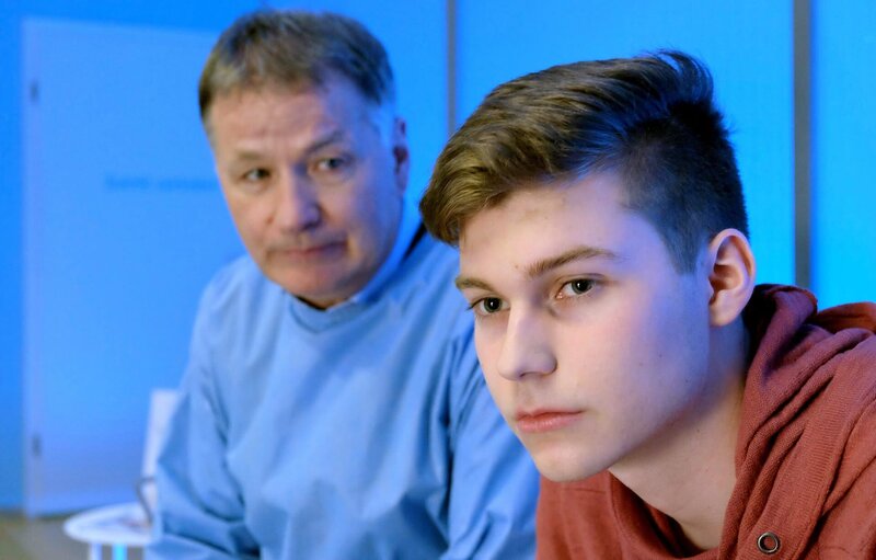 Bastian Heilmann (Johann Lukas Sickert, rechts) geht es nicht gut. Er hat ein Auto gerammt und die Fahrerin liegt nun in der Sachsenklinik. Dr. Roland Heilmann (Thomas Rühmann) versichert ihm zwar, dass der Zustand der Patientin nichts mit dem Unfall zu tun hat, doch nichtsdestotrotz hat Bastian Fahrerflucht begangen und sollte sich stellen. – Bild: BR/​MDR/​Sebastian Kiss