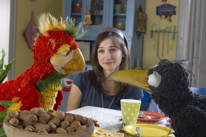 Papagei Loro ist ein echt schräger Vogel und will Siebenstein (Henriette Heinze) und dem Raben Rudi seine Kunststücke vorführen, zum Beispiel Nässe knacken mit dem Schnabel. – Bild: ZDF/​Christiane Pausch
