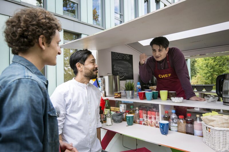 Checker meets Checker: Direktor Chung (Ill-Young Kim, mitte) führt Checker Julian (Julian Janssen, links) am Einstein Gymnasium herum. Dabei mischt sich Orkan (Flavius Budean, rechts) immer wieder in ihre Gespräche ein. – Bild: MDR/​Saxonia Media/​Felix Abraham