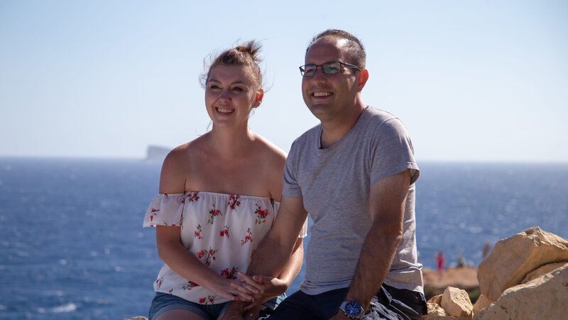 Melissa Shafrir (L) and Avi Shafrir (R) sitting on the rocks with a beautiful view of the Mediterranean Sea, during their big interview about the reasons why they moved to Mellieha, Malta, as seen on Mediterranean Life – Bild: Scripps Networks