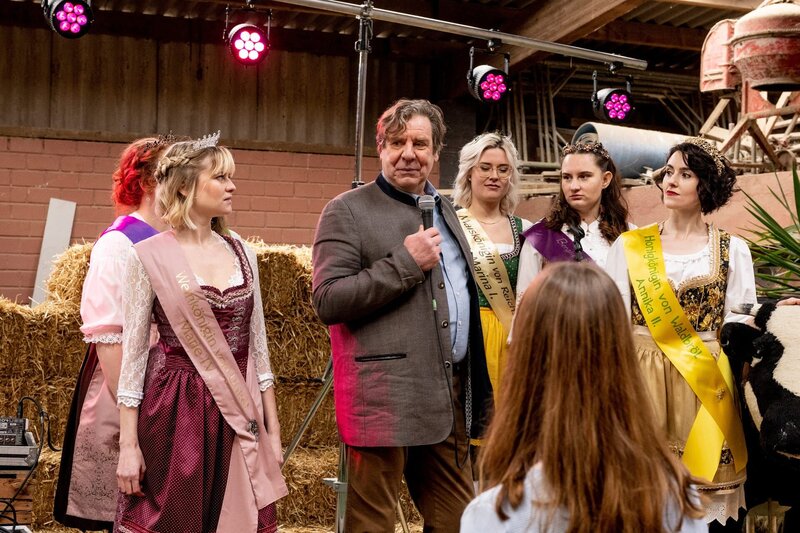 Friedel Broschinski (Uwe Rohde, 3. v. l.), der Vorstand des Gemeinderats, gerät unter Druck: Laut der Weinkönigin von Unkel, Marie Neffgen (Henrike Fehrs, 2.v.l.) äußerte er sich bei der letzten Bauernmesse unangemessen und wurde dabei von dem Mordopfer gefilmt. (Komparsen im Bild) – Bild: ZDF und Martin Rottenkolber