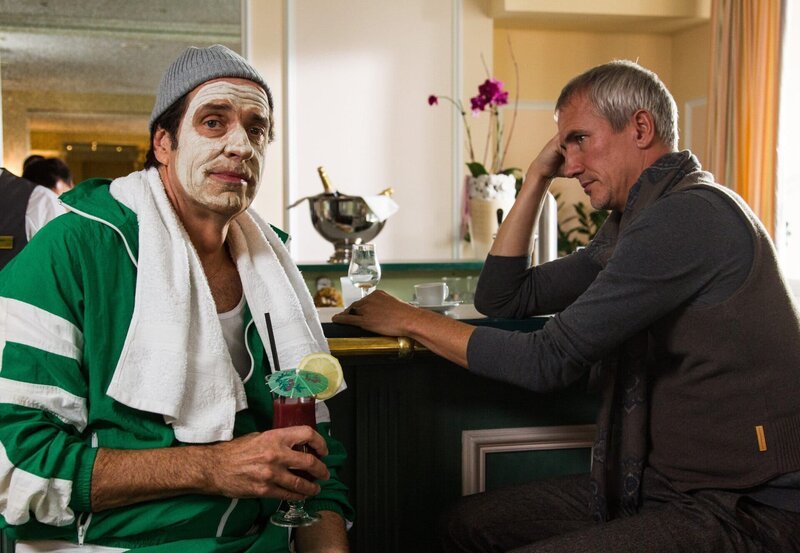 Staller (Helmfried von Lüttichau, r.) setzt sich mit orangefarbener Feuchtigkeitsmaske und Cocktail zu Robert Jung (Markus Böker, r.) an die Bar. Robert Jung erzählt ihm, dass sich Ute komisch benimmt und er sich nicht mehr sicher ist, ob er mit ihr die Beziehung weiter führen möchte. – Bild: ARD/​TMG/​Chris Hirschhäuser