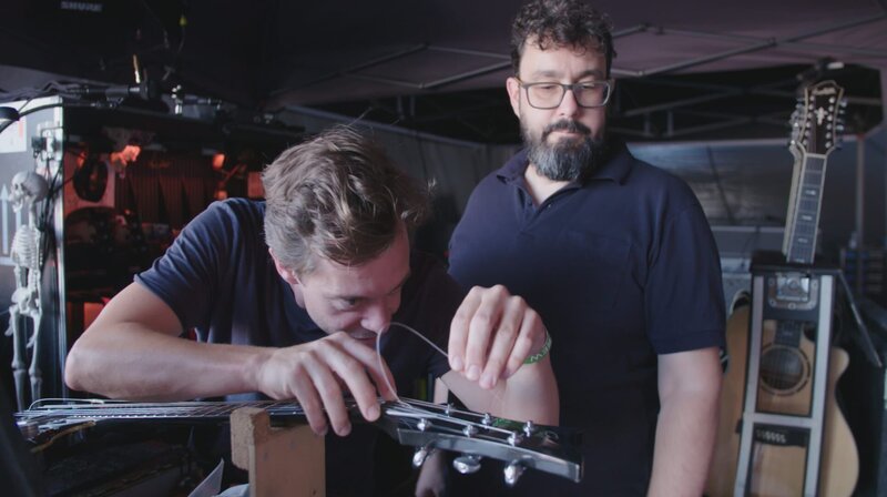 Checker Tobi darf eine Saite für den Gitarristen der Band „Die Ärzte“ aufziehen. – Bild: BR/​megaherz gmbh/​Martin Groß