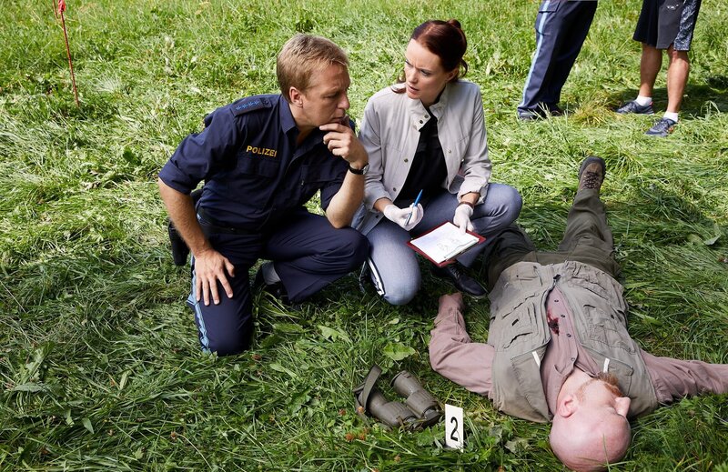 Pathologin Mai (Sina Wilke, r.) klärt Hauptmeister Mohr (Max Müller, l.) über die Todesursache und den Todeszeitpunkt im Mordfall des Försters Denninger (Komparse) auf. – Bild: ZDF und Bojan Ritan