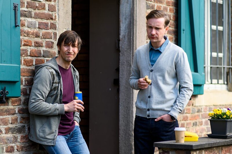 Die Zollbeamten Benno Löhken (Hendrik Heutmann, l.) und Dirk Sinning (Max Rothbart, r.) genießen ihre Mittagspause vor dem Zollamt, als sie unangekündigten Besuch bekommen. – Bild: ZDF und Marius Becker
