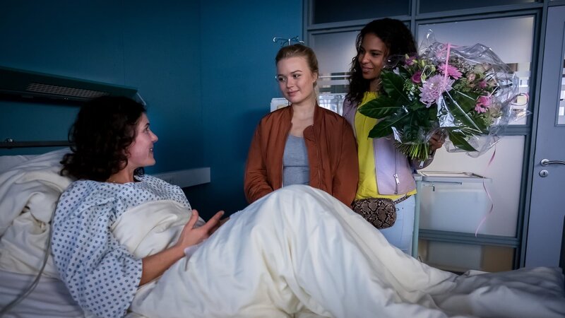 Paulina (Anna-Isabel Hinz, M.) und ihre Freundin Tamina (Souhaila Amade, r.) besuchen ihre Schulleiterin (Yasmina Djaballah, l.) und hoffen, dass sie bis zum Abiball wieder genesen ist. – Bild: ZDF und Boris Lasewen