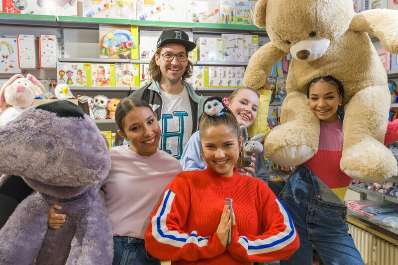 Die TanzAlarm Kids und herrH suchen im Spielzeugladen nach dem richtigen Geschenk. – Bild: KiKA/​MingaMedia/​Ron Bergmann