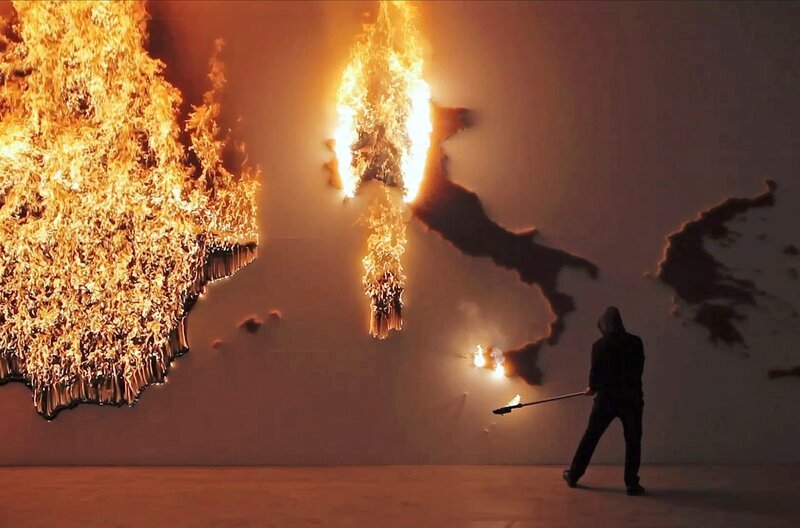 Dass die Welt buchstäblich in Flammen steht, zeigt die Performance des Künstlerkollektivs Claire Fontaine. – Bild: Studio Claire Fontaine/​“P.I.G.S.“-Projekt