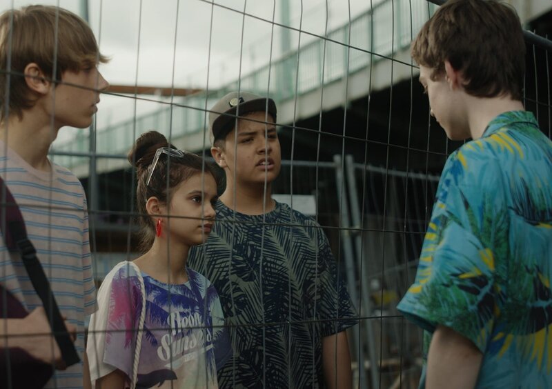 Aaron wird von seinen Freunden beim Urlaubs-Fake erwischt. (v.l.n.r.: Alex (Paul Bohse), Berfin (Artemis Kostopoulou), Tim (Marc Aurelius Lansen), Aaron (Philip Müller)) – Bild: KiKA/​2021 eitelsonnenschein