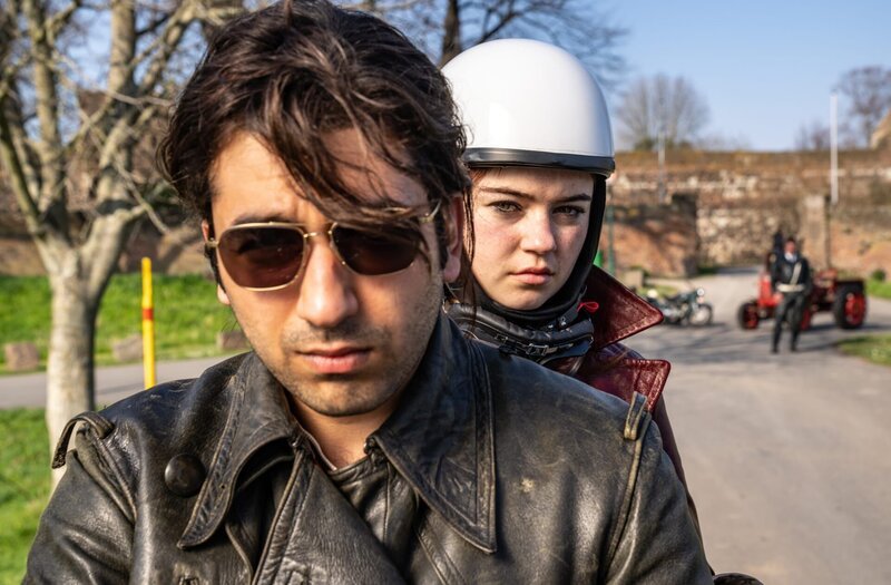 Bijan (Omid Memar) und Betty (Ella Lee) fahren mit dem Motorrad und werden von Schneider (Raphael Westermeier) und seinen Kollegen angehalten und überprüft. – Bild: ZDF und WDR/​UFA Fiction/​Wolfgang Ennenbach