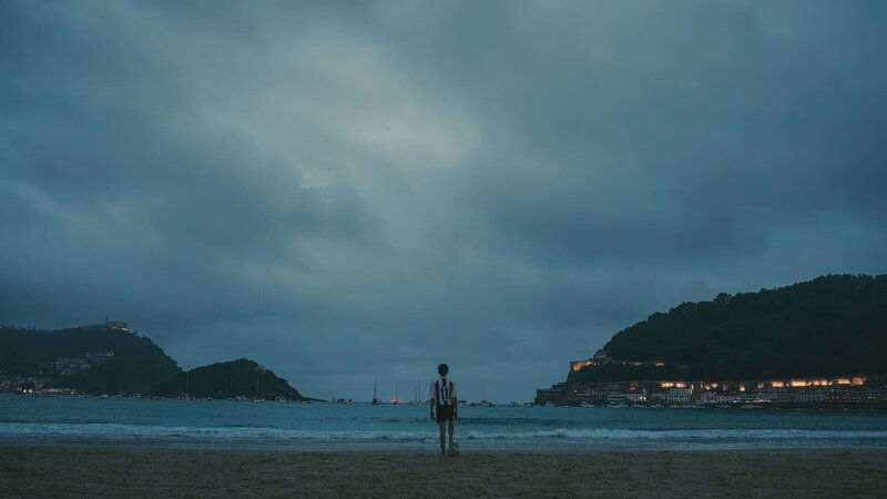 Ein Junge in einem Fußballtrikot steht auf einem Ball am Meer. – Bild: Beta Entertainment Spain 2023