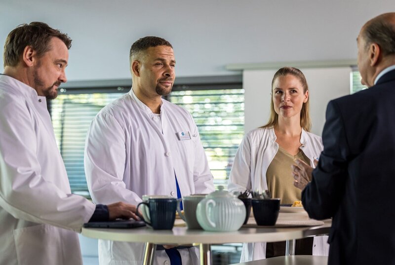 Wolfgang Berger (Horst Günter Marx, r.) verkündet die Aufteilung der finanziellen Förderung für die Abteilungen seiner Oberärzte Dr. Marc Lindner (Christian Beermann, l.), Dr. Matteo Moreau (Mike Adler, 2.v.l.) und Dr. Julia Berger (Mirka Pigulla, 2.v.r.). – Bild: ARD/​Michael Kremer