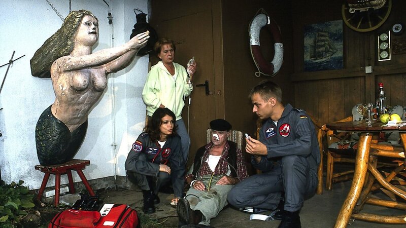 Hulda (Eva Zlonitzky, 2.v.l.) hat ihren bewusstlosen Nachbarn Göhlen (Karl Heinz Choynski, 2.v.r.) gerade noch rechtzeitig entdeckt. Sie weiß genau, was zu tun ist, denn auch sie wurde vor Kurzem mit einem Herzinfarkt von den Rettungsfliegern Maren (Gerit Kling, l.) und Torsten (Tom Wlaschiha, r.) abgeholt. – Bild: ZDF und Boris Laewen