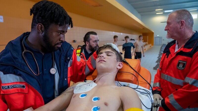 Dr. Schmidt (Joel Williams, l.) kümmert sich um Frederik Tomke (Juls Luis Serger, M.), der beim Apnoetauchen einen Blackout erlitten hat. – Bild: ZDF