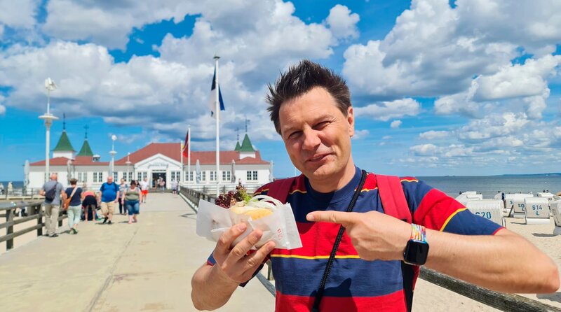 André Gatzke isst ein Fischbrötchen auf der Seebrücke. – Bild: WDR/​Alice Tschöke