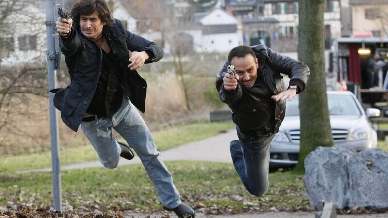 Ben (Tom Beck, li.) und Semir (Erdogan Atalay) kommen am Hausboot an und geraten unvermittelt in eine Schießerei … – Bild: TVNOW /​ Guido Engels