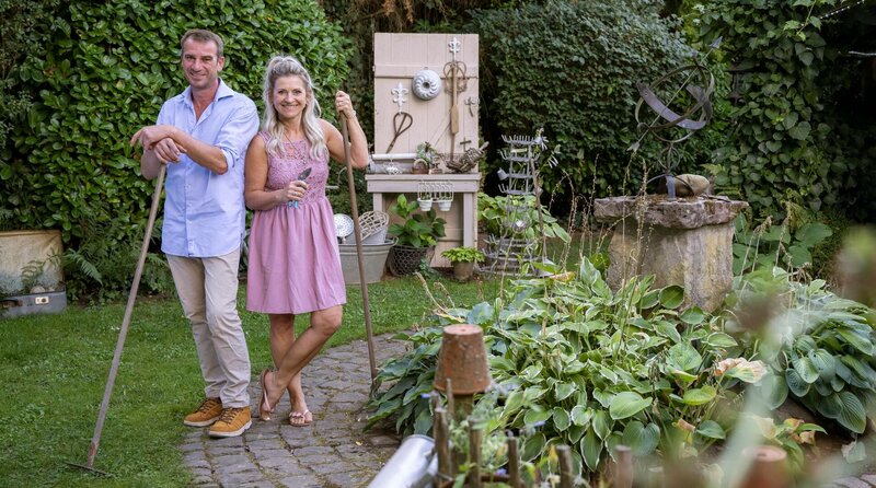 In der fünften Folge lädt „Deko-Queen“ Alexandra Straßburger aus Saarbrücken in ihren Garten. Auf 2000 Quadratmetern lebt die begeisterte Flohmarktbesucherin ihren ganz persönlichen Gartentraum. „Der Garten ist so vielfältig wie wir“ sagt Alexandra und hat so neun extrem unterschiedlich gestaltete grüne Zimmer erschaffen von der Wellnessoase über einen streng geometrisch bepflanzten „Klostergarten“ bis hin zum romantisch verspielten Rosengarten. – Alexandra Straßburger (r) im Garten in Saarbrücken mit ihrem Mann Mike. – Bild: WDR/​Melanie Grande