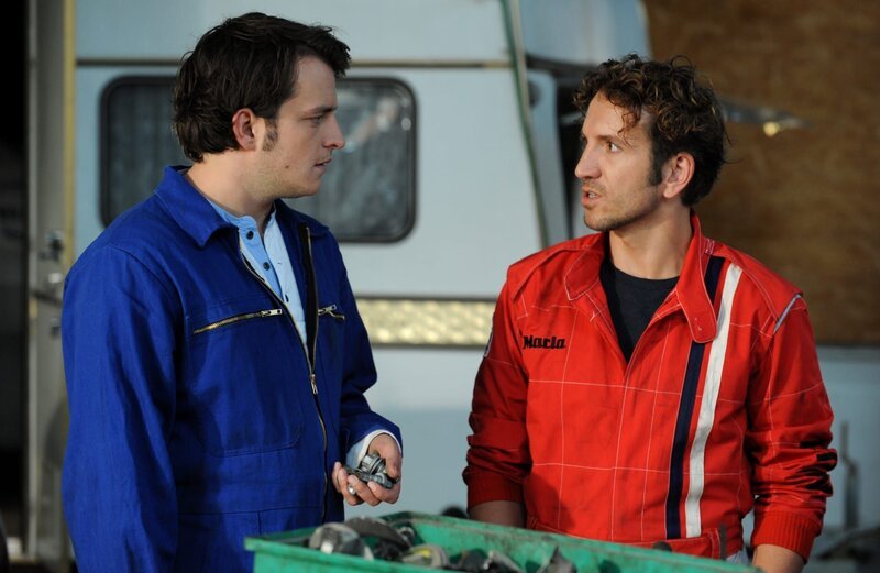 Lex erklärt Flori, wie der vermeintliche Schaden bei einem der Wagen zustande gekommen ist. Von links: Florian Brunner (Tommy Schwimmer) und Lex (Sebastian Gerold). – Bild: BR/​Marco Orlando Pichler
