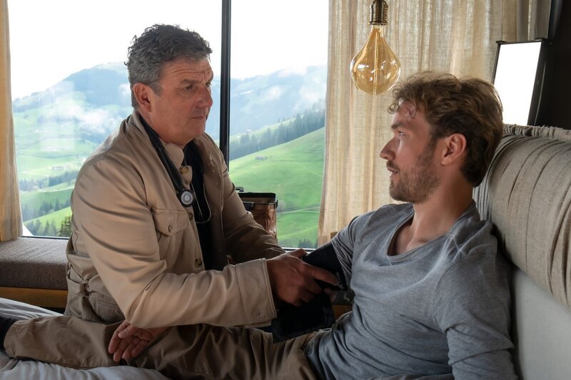 Nach seinen Ausfallerscheinungen untersucht Dr. Martin Gruber (Hans Sigl, l.) Jan Seidl (Max Woelky, r.) und ahnt, dass sein Patient ihm etwas verheimlicht. – Bild: ZDF und Erika Hauri