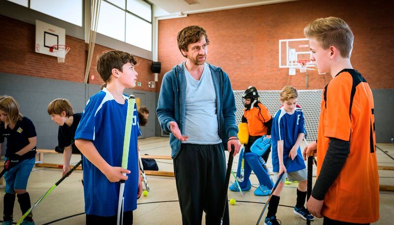 Hockeytrainer John (Andreas Nickl, Mitte) versucht, den Streit zwischen Ramin (Jann Piet, li.) und Tom (Vincent Grages, re.) zu schlichten. – Bild: NDR/​Boris Laewen