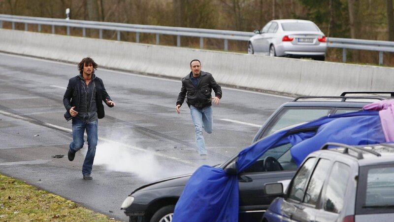 Ben (Tom Beck, li.) und Semir (Erdogan Atalay) verfolgen den Gangster Andreas Keller. Der kracht in einen Anhänger, hebt ab, und landet im Gegenverkehr. – Bild: TVNOW /​ Guido Engels