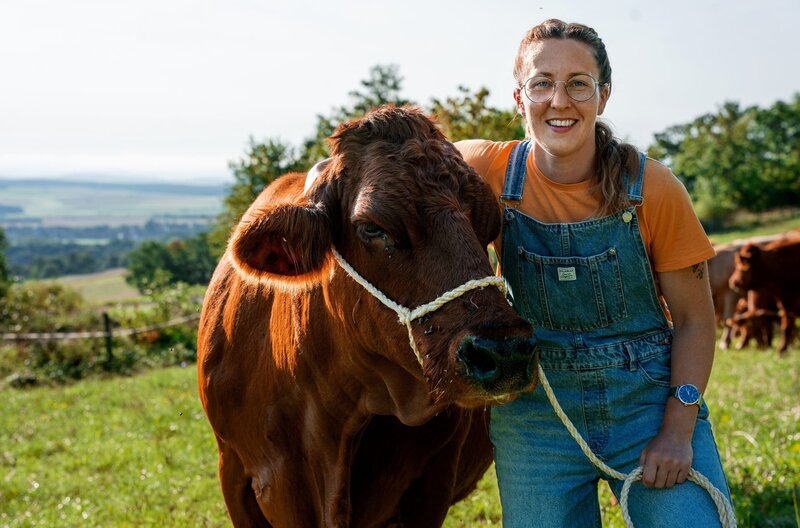 Nadine wollte eigentlich nicht Landwirtin werden. Sie ist gelernte Metzgereifachverkäuferin. Dann lernte sie ihren Mann kennen und heute führen die beiden den Biohof im unterfränkischen Landkreis Rhön-Grabfeld gemeinsam. 70 Rinder der vom Aussterben bedrohten Rasse des Fränkischen Gelbviehs in Mutterkuhhaltung sind das Hauptstandbein des Hofes, auf dem drei Generationen leben. Nadines Wunsch ist es, andere Menschen von guter Tierhaltung und bewusstem Fleischkonsum zu überzeugen. – Bild: BR/​megaherz gmbh/​Moritz Sonntag