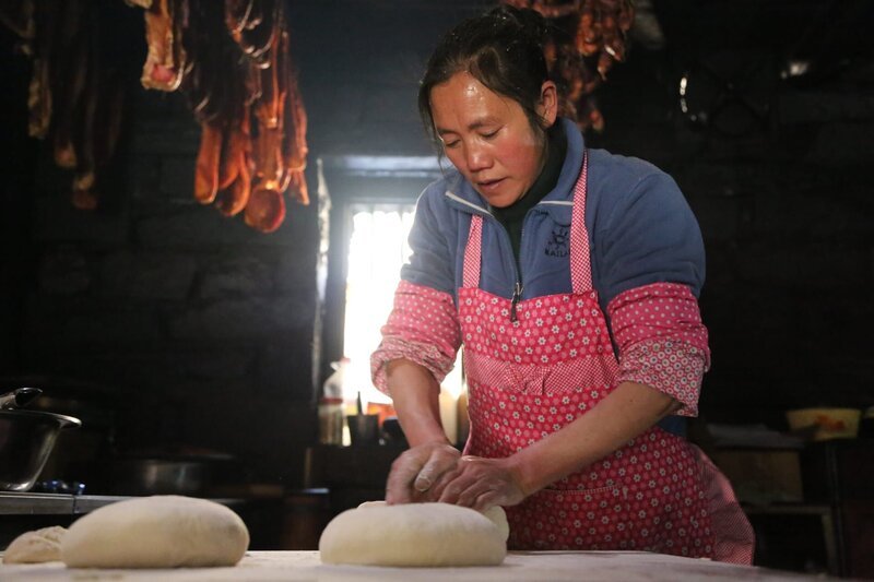 Mrs. Wang makes momo – bread – with smoked yak meat and pork hanging in the background. – Bild: National Geographic /​ Liu Fang