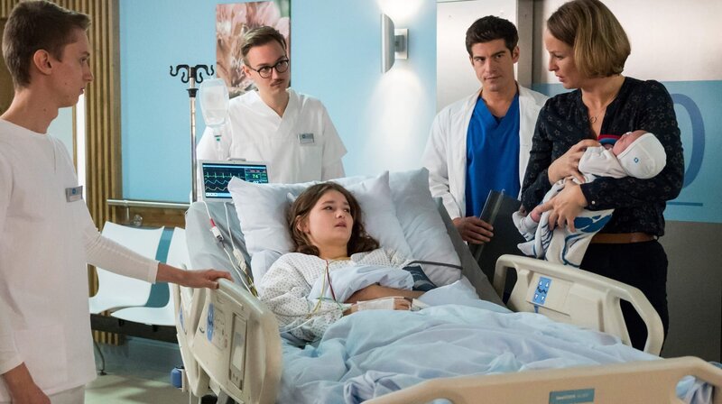 Nina Sander (Lara Joy Körner, r.) und Ben (Philipp Danne, 2.v.r. mit Komparsen) hoffen, dass Hermine (Greta Bohacek, M.) ihre keine Tochter doch noch annehmen wird. – Bild: ARD/​Jens Ulrich Koch