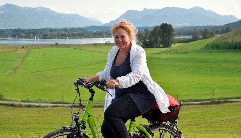 Bayerisches Fernsehen TRAUMPFADE, „Rund um den Chiemsee“, am Donnerstag um 20:15 Uhr. Auf dem Fahrrad erkundet die gebürtige Chiemgauerin Gertraud Dinzinger (im Bild) den geliebten See ihrer Kindheit neu, nimmt sich Zeit für spontane Begegnungen und ungeplante Abstecher und entdeckt dabei die verborgenen, zauberhaften und kuriosen Seiten des „bayerischen Meers“ und seiner Umgebung. – Bild: BR/​Sabine Reeh