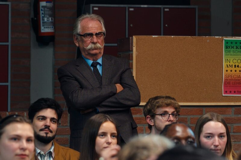 Schulleiter Udo Brückmann (Henning Krautmacher) hört sich die Wahlkampfreden der Kandidaten Ben und Rick an, die Konkurrenten bei der Wahl zum Oberstufensprecher sind. – Bild: Philipp Pfeiffer /​ ZDF