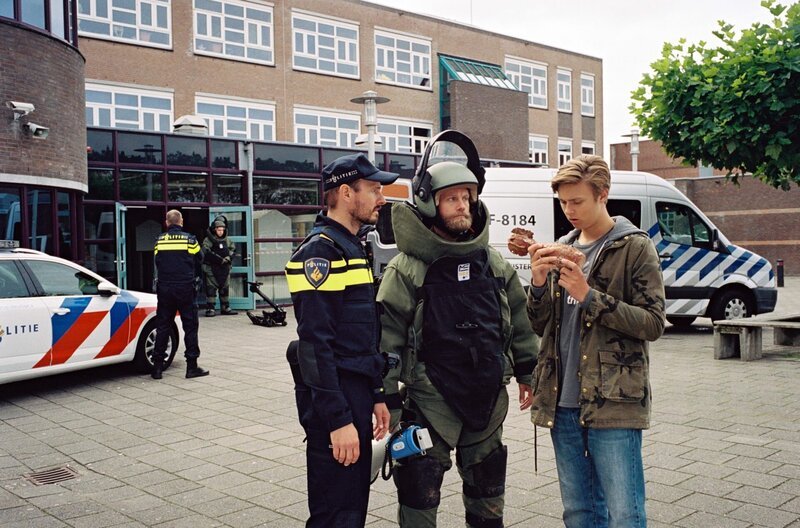 Kees (Ole Kroes, re.) auf dem Schulhof mit der Polizei und dem Bombenspezialisten. – Bild: NDR/​NL Film/​Maurice Trouwborst